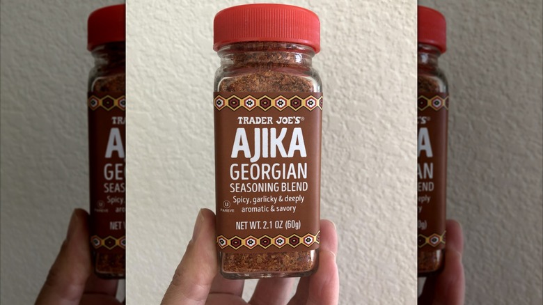 mirrored image of hand holding Trader Joe's Ajika Georgian seasoning jar against white wall