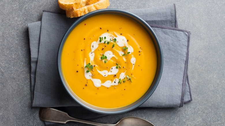 Bowl of carrot soup next to sliced bread and spoon