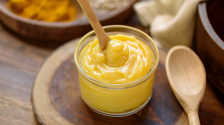 A glass jar of ghee swirled with a small wooden spoon