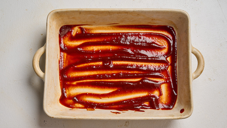 spreading enchilada sauce into casserole dish