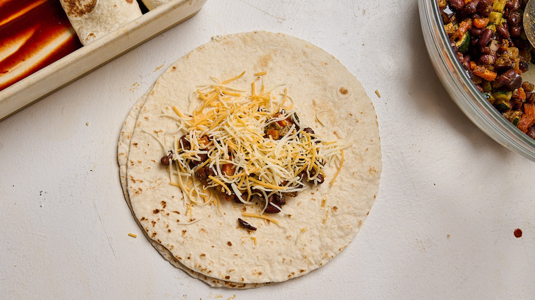 assembling enchiladas with veggies and beans