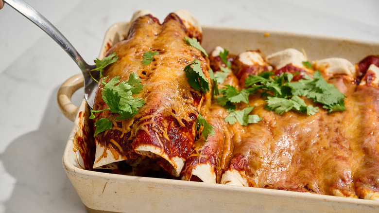 spatula lifting enchiladas out of casserole dish