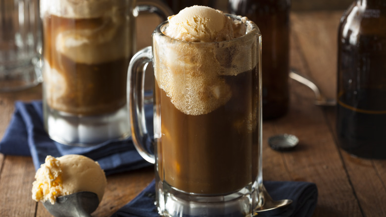 Two root beer floats in large glass beer mugs, sat on blue napkins on a wooden table