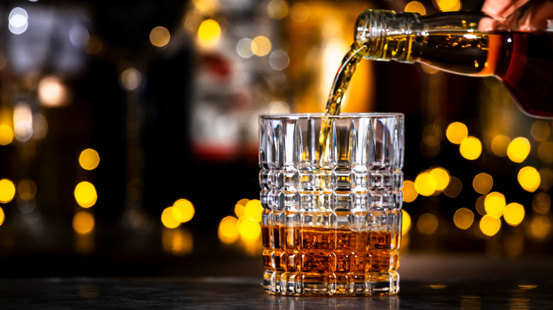 A close-up of rum being poured from a glass bottle into a cube pattern lowball glass.
