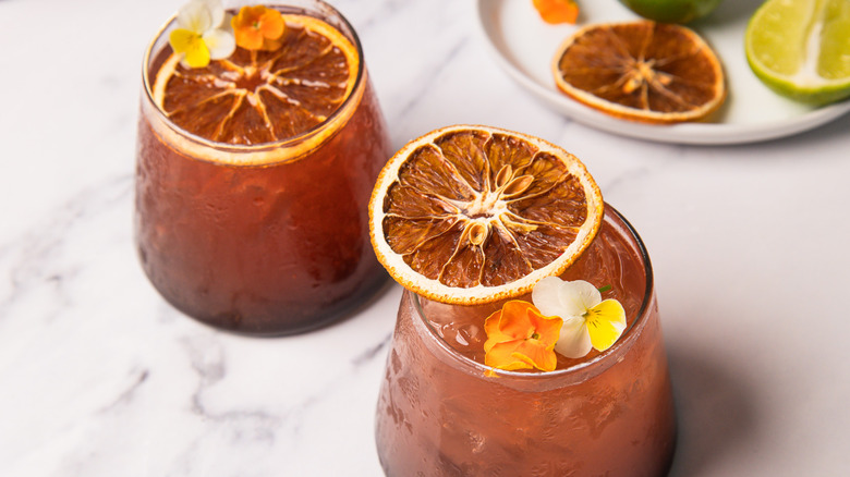 Two blood orange rum sunset cocktails with garnishes in background