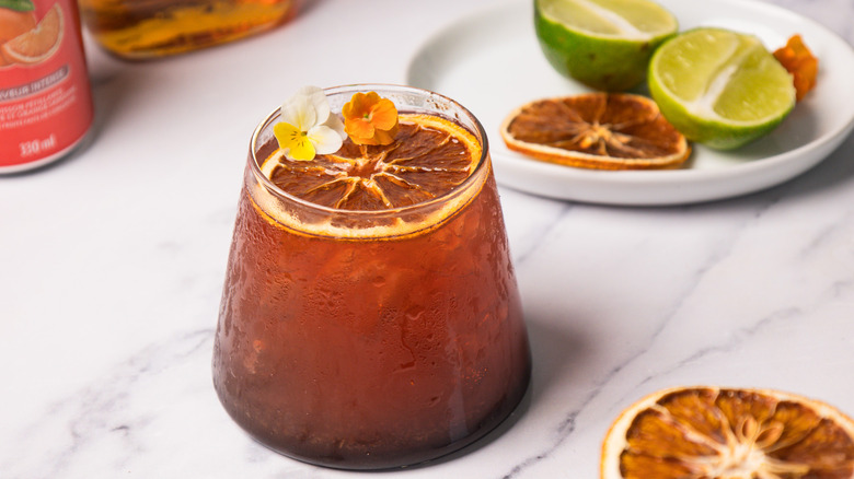 A blood orange rum sunset cocktail with garnishes in background