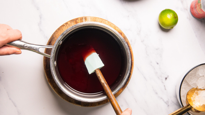 Spatula stirring pomegranate juice and sugar in saucepan