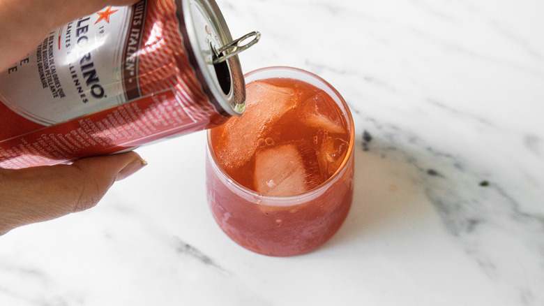 Hand pouring soda from can into glass