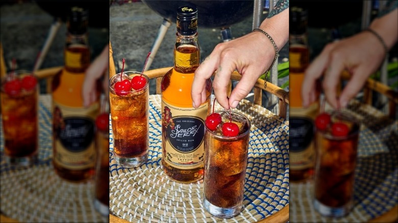 Two cocktails made with Sailor Jerry rum with cherry garnishes, next to a bottle