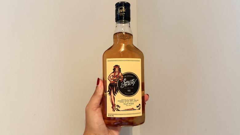 Hand holding a Sailor Jerry pint bottle in front of a neutral background