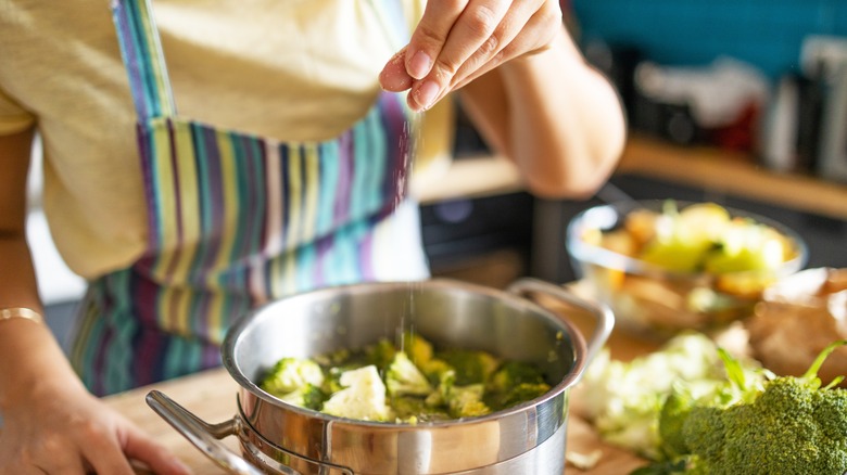 woman seasoning a pot with broccoli