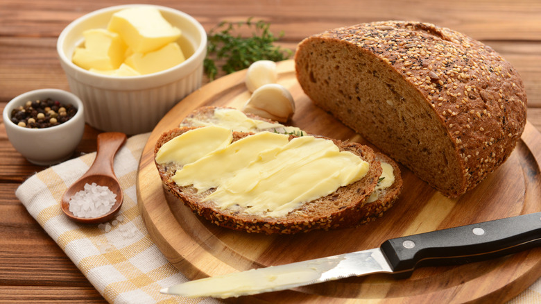 Butter spread on a slice of hearty brown bread with salt and the remaining loaf nearby