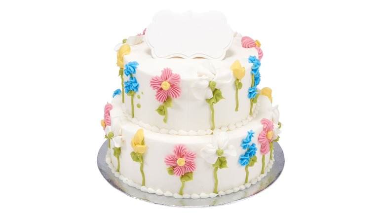 A two-tier cake with white icing and colorful flower designs on white background