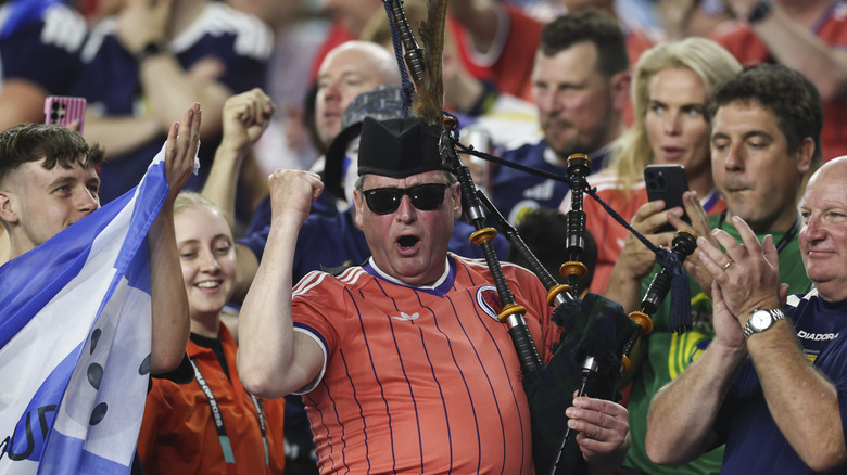 A Scotland fan wearing sunglasses holds up his first while holding the bagpipes while surrounded by other Scotland fans attending the World Cup in Boston