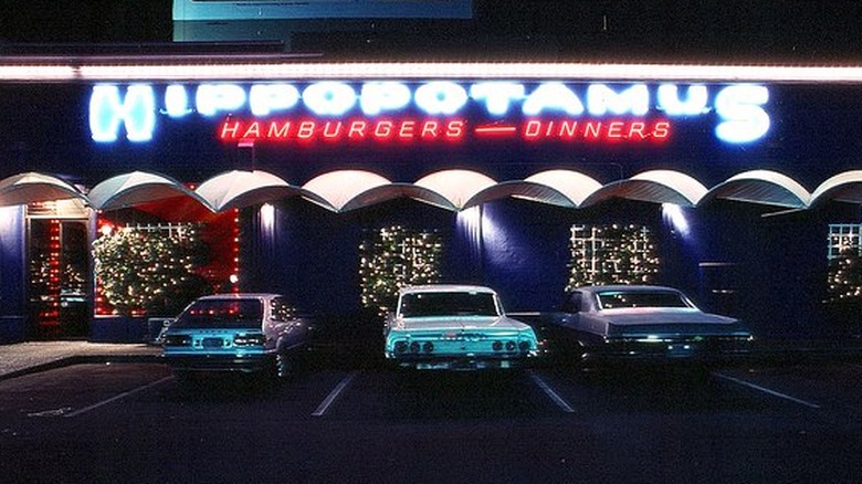 The lit up exterior of Hippopotamus Burger in San Francisco at night with vintage cars outside