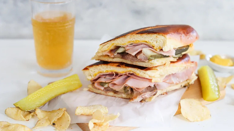 All-Out Cuban Sandwich with chips and pickles on wooden board