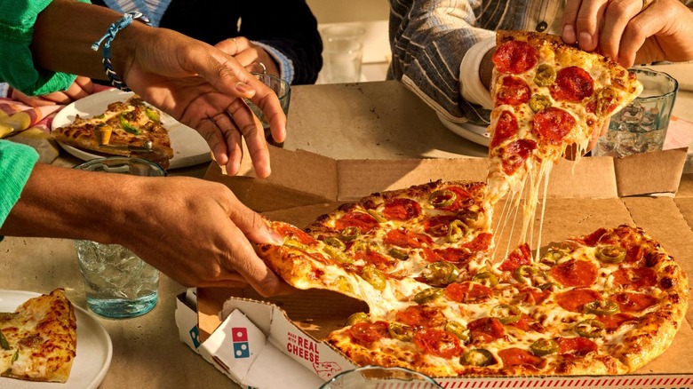 Hands picking up slices of Domino's pepperoni pizza from the box