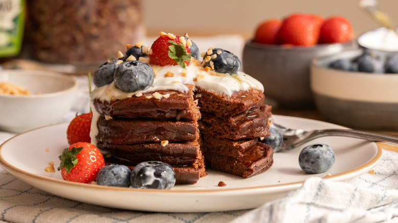 Stack of high protein chocolate pancakes with slice cut out and fruits on top
