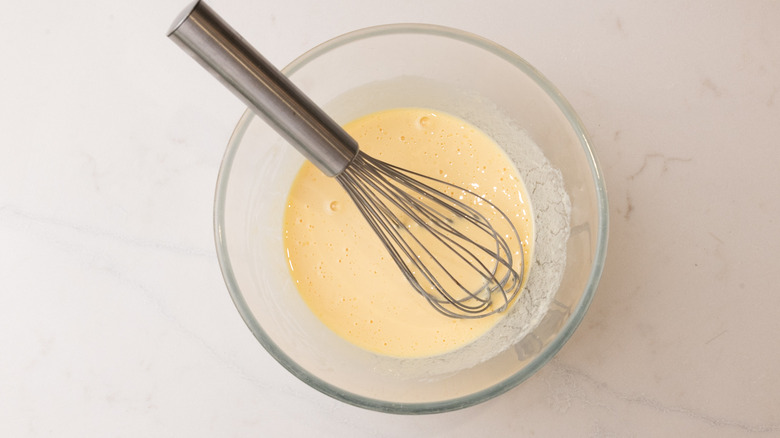 whisked wet pancake ingredients in glass bowl with whisk