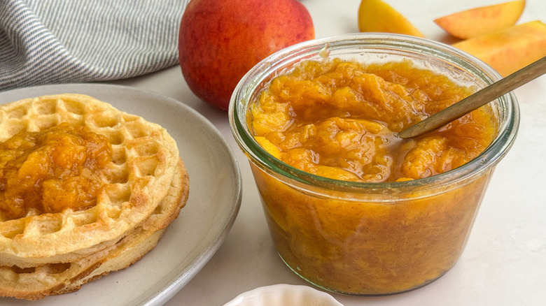 Peach sauce in glass bowl with spoon, next to plate of waffles