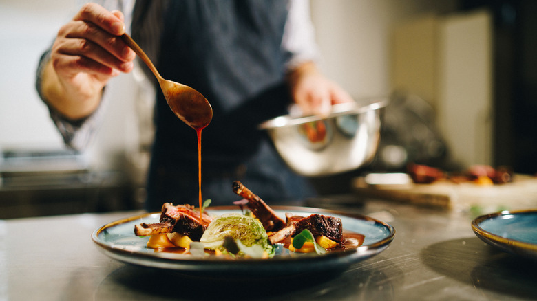 Chef finishing a plate of food with a drizzle of sauce from a spoon