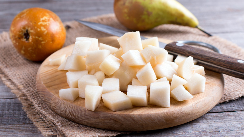 cubed pears on a cutting board with a knife and whole pears in the background