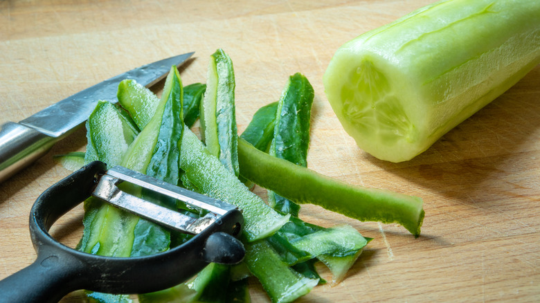 A peeled cucumber alongside a peeler.