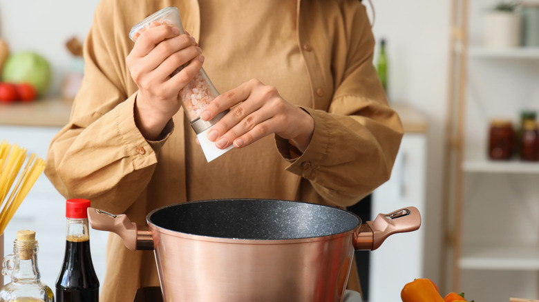 seasoning a pan of soup in kitchen