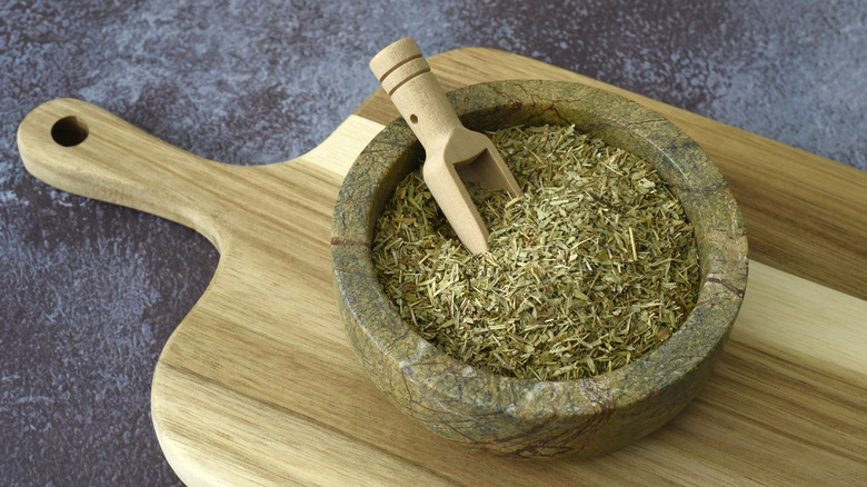 A marble bowl filled with dried winter savory and a wooden scoop