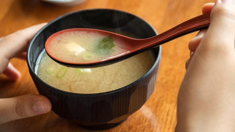 A hand scoops a spoon of miso soup.