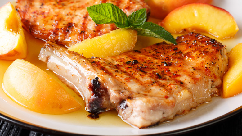 pork chops and peaches on a plate served with a sauce and mint sprig
