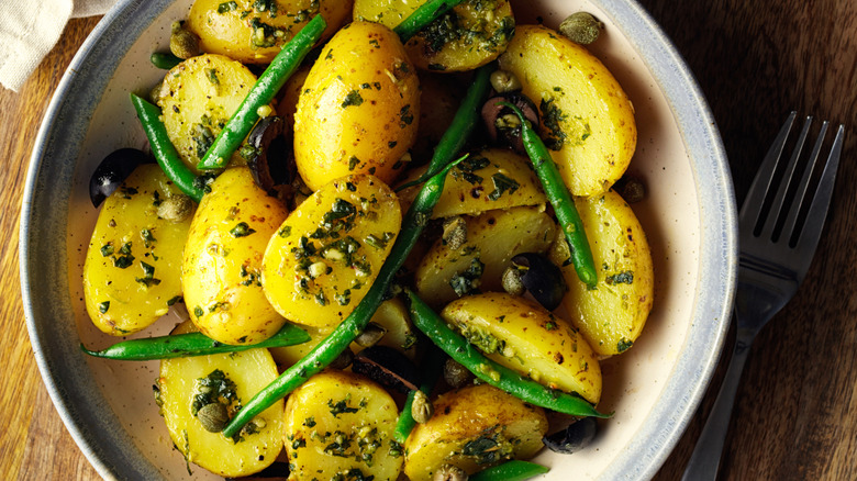 A bowl of golden potato salad lightly dressed with herbs and string beans