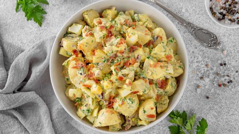 A bowl of creamy potato salad with bacon and fresh herbs