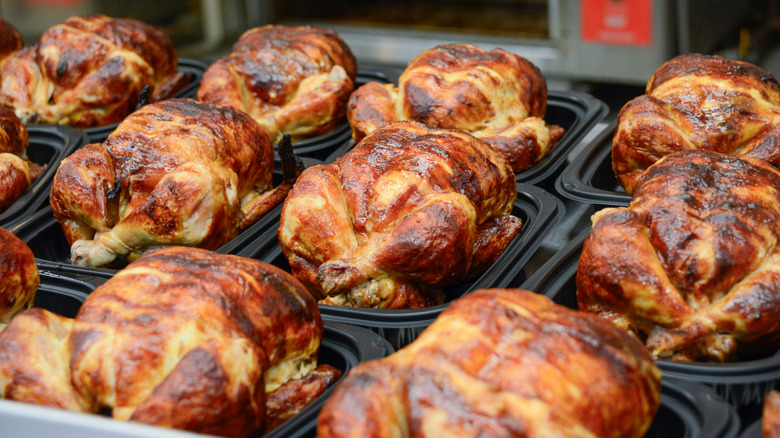 Rotisserie chickens in uncovered plastic containers lined up at a store