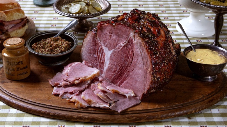 Half a Kurobuta ham, roasted and sliced on a platter with mustards in bowls