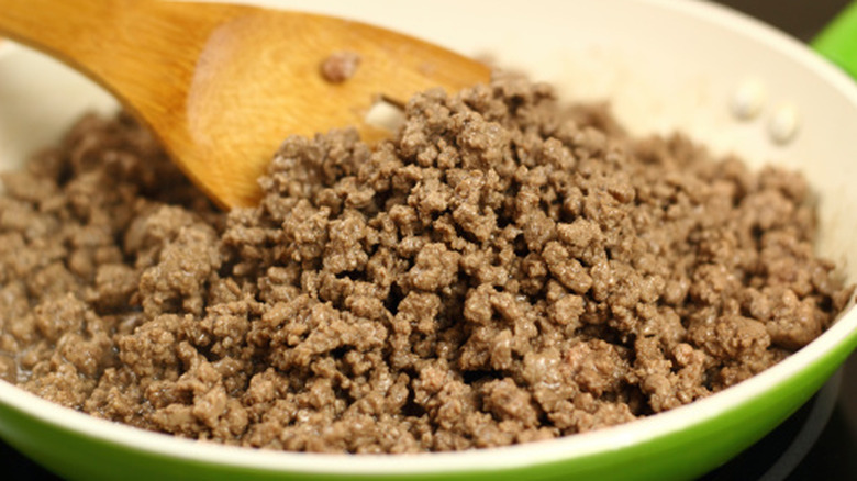 A pan of cooked ground beef being stirred with a wooden spoon