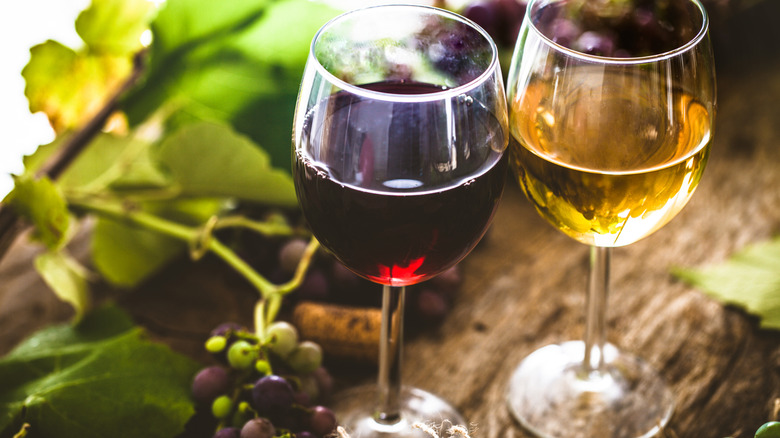 A glass of red wine next to glass of white wine on a wooden table next to grape vine