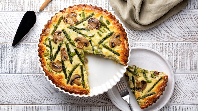 aerial photo of a sliced mushroom and asparagus quiche on white plate