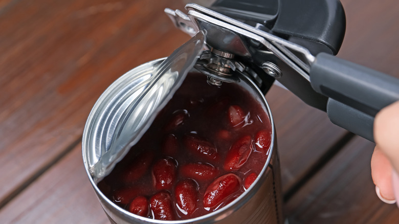close up of can opener opening tin of kidney beans