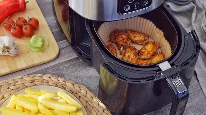 air fryer cooking wings with fries and tomatoes