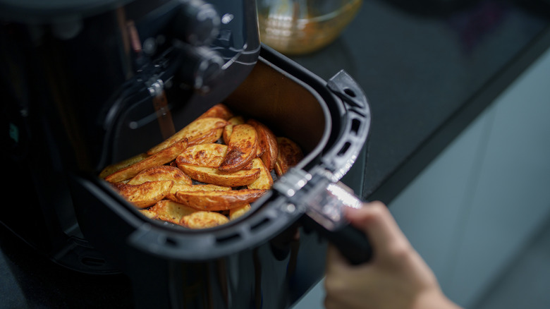 hand opening an air fryer with crispy potato wedges