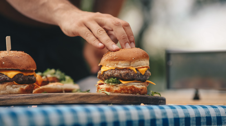 Hand pressing down on homemade cheeseburgers