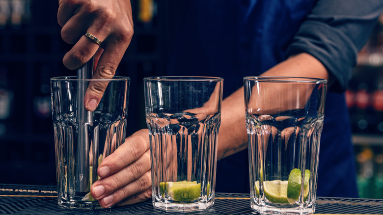 bartender muddles lime pieces at bottom of glass