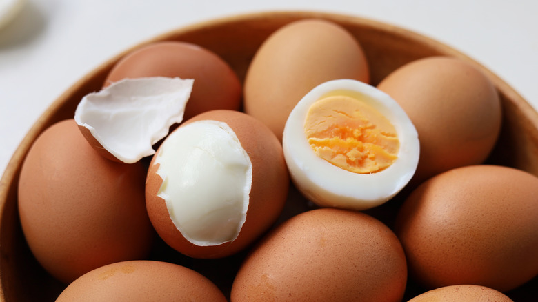 Sliced hard boiled in egg in bowl with unpeeled eggs