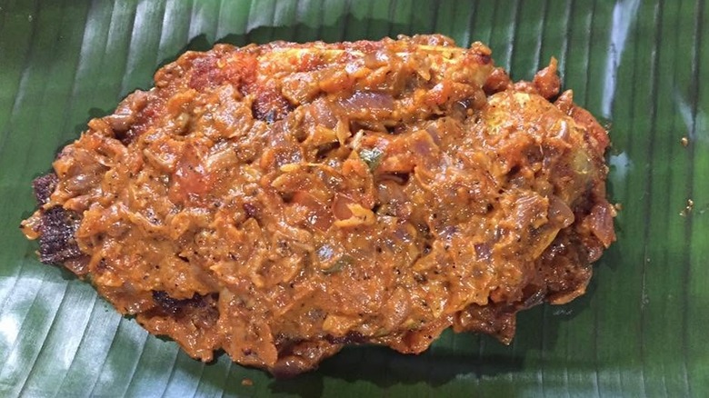 Pearl spot fish in banana leaf topped with onions and sauce