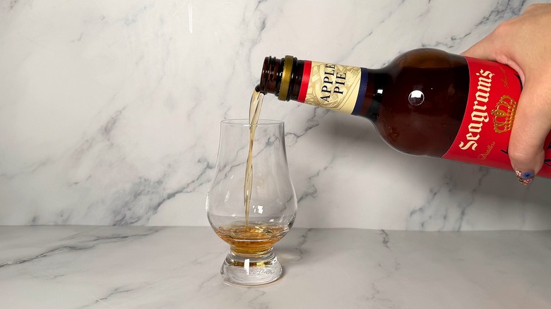 Hand pouring bottle of Seagram's Apple Pie Whiskey into glencairn