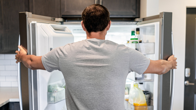 person looking in open refrigerator with food