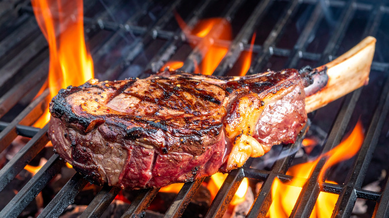 a tomahawk steak on a grill with flames coming up
