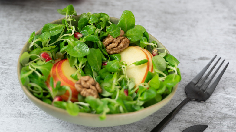 Bowl of salad with lamb's lettuce or mache, sliced apples, and walnuts next to black fork