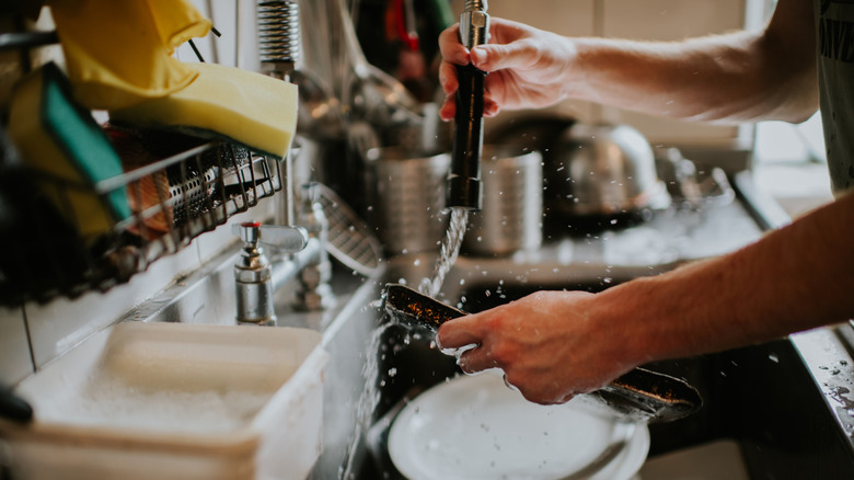 A man washing a pan and other dishes in a commercial kitchen sink